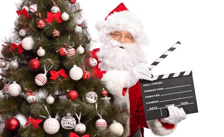 Santa Claus posing with a clapperboard and Christmas tree to film holiday video campaigns.