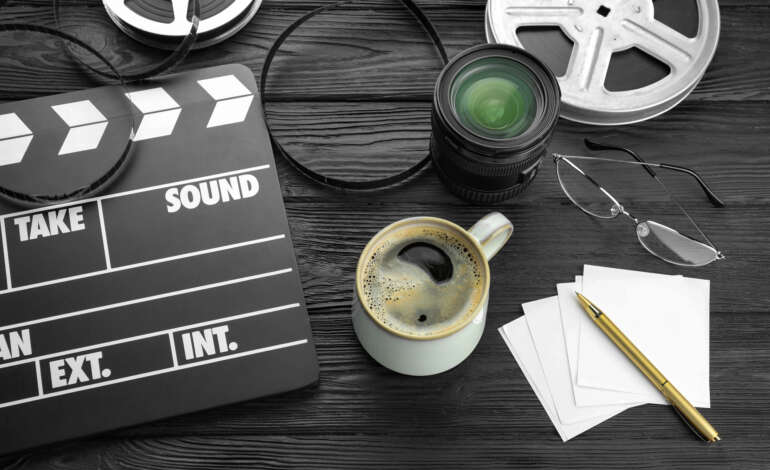 Camera lens, film reels and movie clapper on a black table.