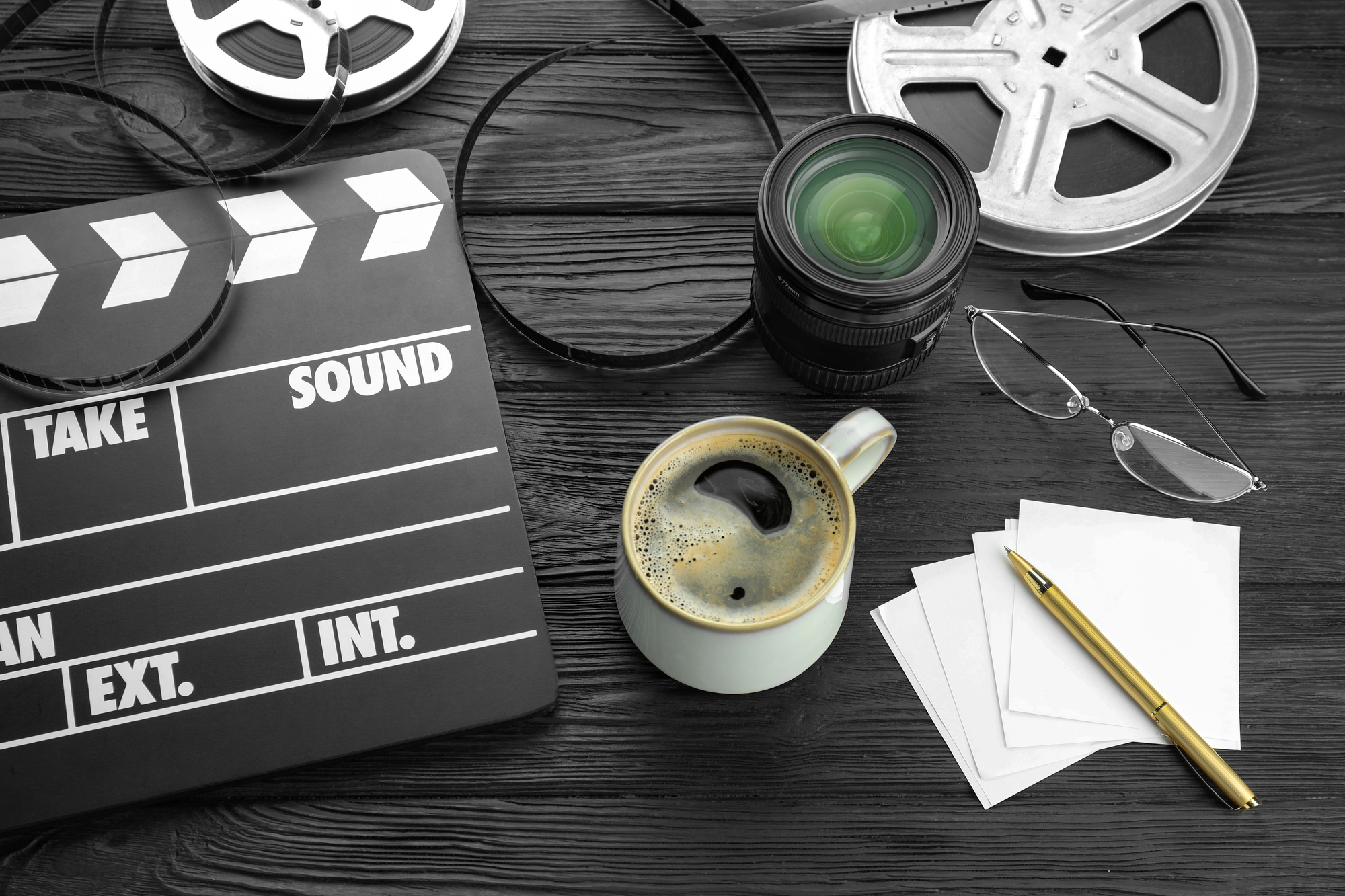 Camera lens, film reels and movie clapper on a black table.