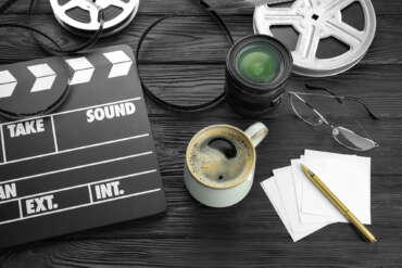 Camera lens, film reels and movie clapper on a black table.