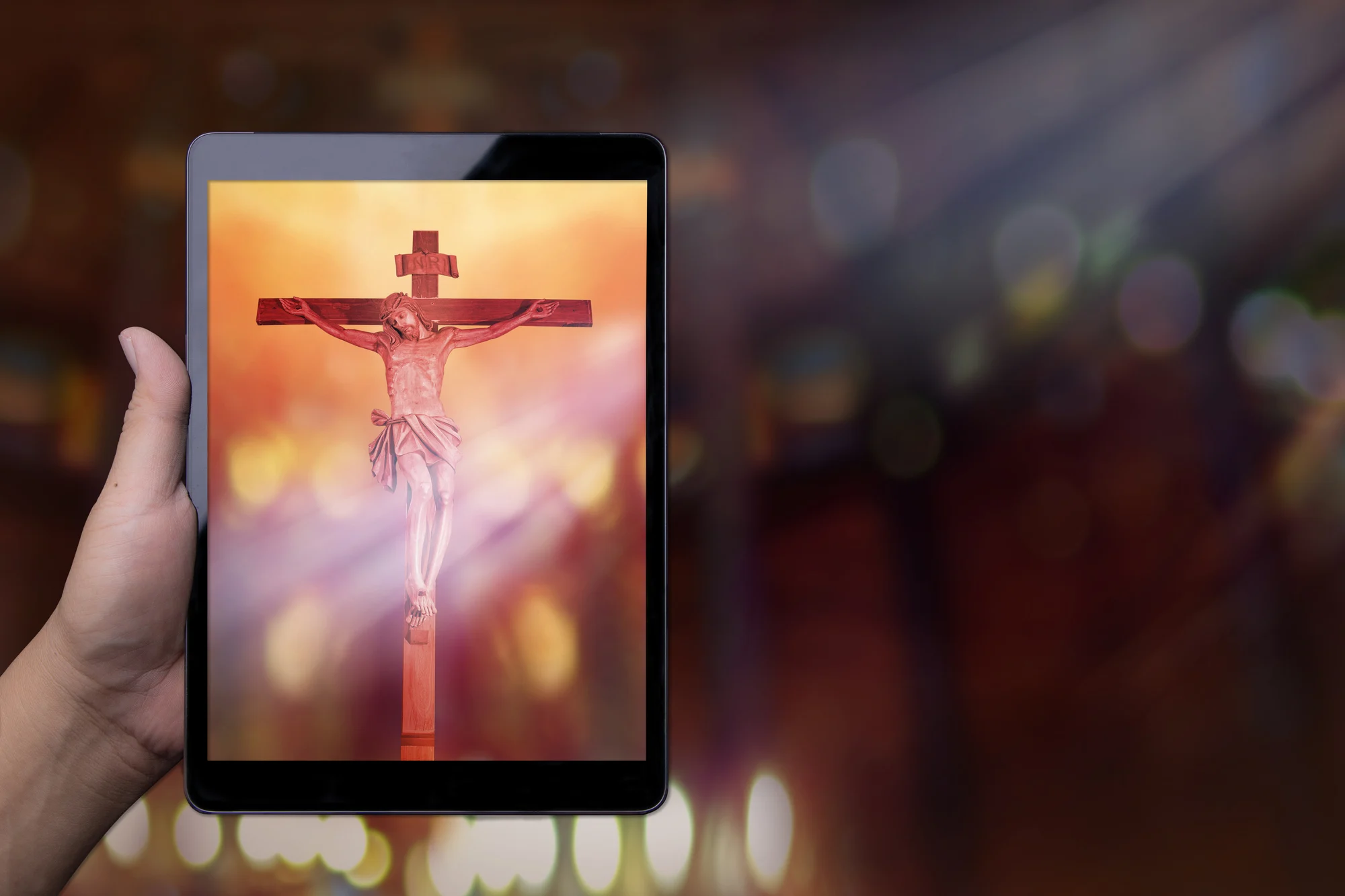 Hand holding a tablet displaying a picture of Jesus on the cross.